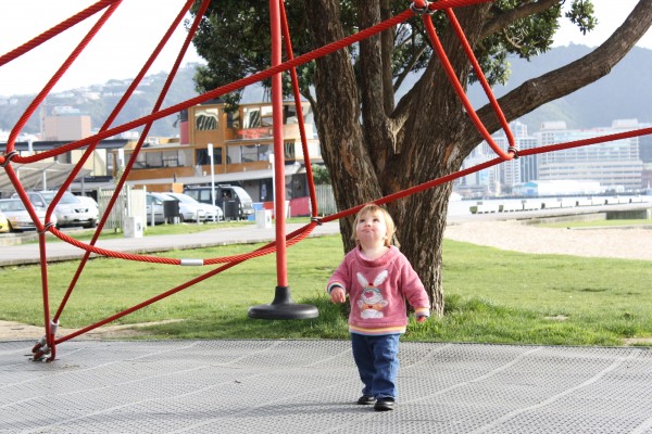 Alice gazing up at her sister Sophie on the big pyramid climbing frame at Oriental Parade