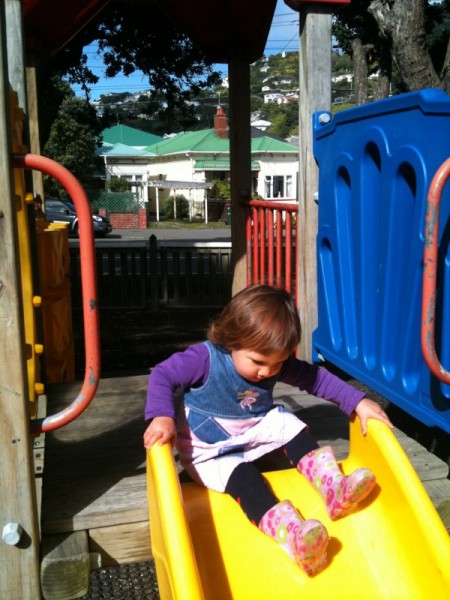 Alice zipping down a slide in her gumboots