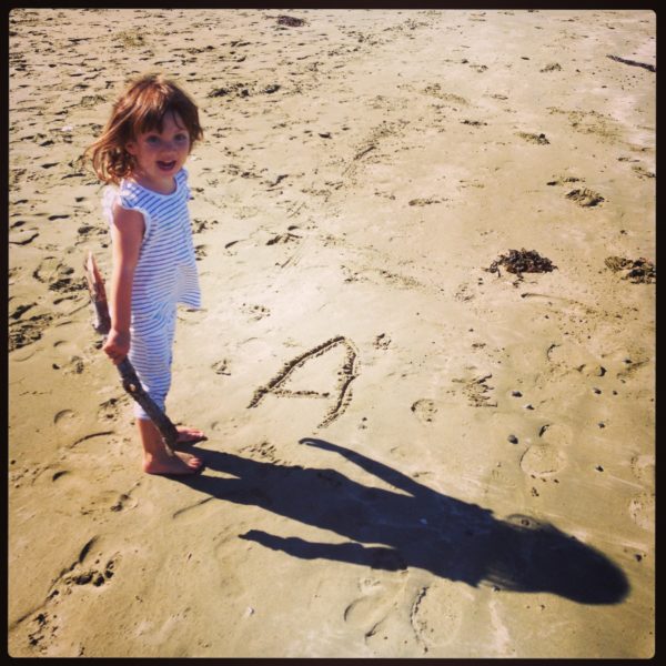 Alice writing the first letter of her name in the sand at Lyall Bay beach